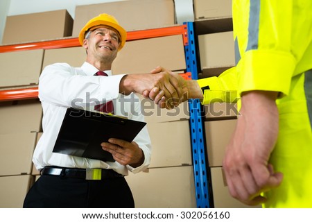 Happy Manager Holding Clipboard Shaking Hands With Warehouse Worker