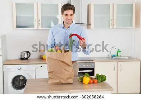 Happy Young Man Standing With Grocery Bag In Kitchen Room