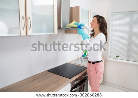 Young Woman Cleaning Cooker Hood With Rag And Detergent In Kitchen