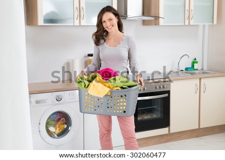 Happy Woman Carrying Laundry Basket In Kitchen Room