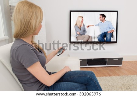 Young Woman Changing Channel With Remote Control In Front Of Television