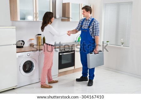 Young Male Repairman Shaking Hands With Happy Woman In Kitchen
