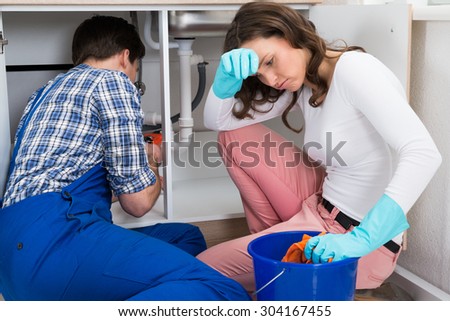 Handyman Repairing Sink Pipe While Exhausted Woman Squeezing Cloth In Bucket