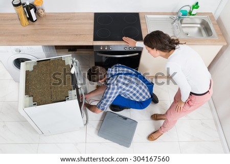 Young Woman Looking At The Work Of Repairman Repairing Dishwasher In Kitchen