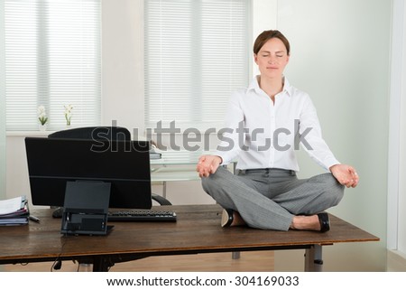 Young Businesswoman Doing Yoga On Wooden Desk In Office