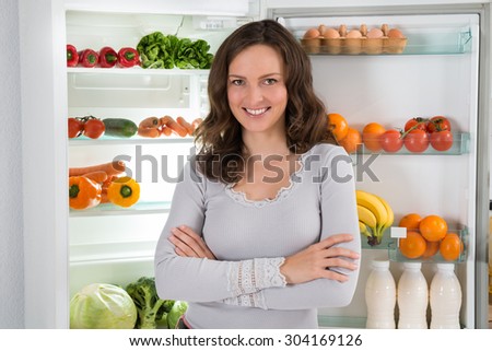 Young Happy Woman With Armcrossed In Front Of Open Fridge With Healthy Food