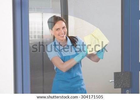 Young Happy Female Janitor Cleaning Glass With Rag