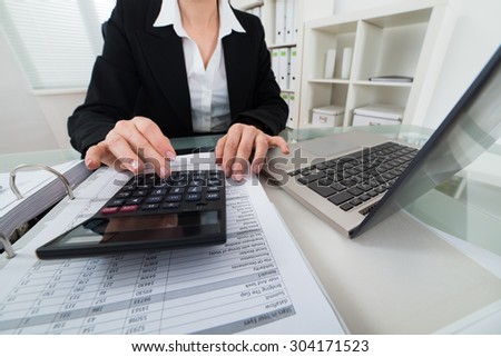 Close-up Of Businesswoman Calculating Invoice With Calculator