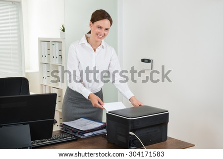 Young Female Secretary Inserting Paper In Printer At Desk