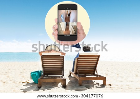 Man With Wife At Beach Looking At Security System On Mobile Phone