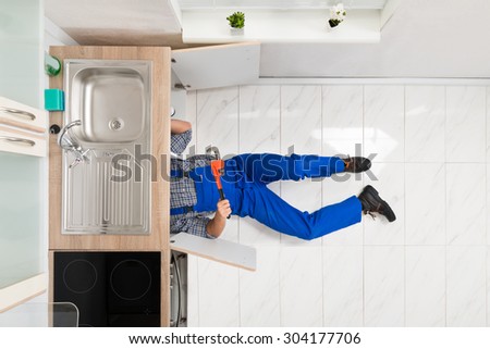 Worker Lying On Floor Repairing Kitchen Sink With Adjustable Wrench