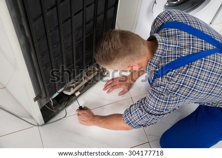 Young Male Repairman Making Refrigerator Appliance In Kitchen Room