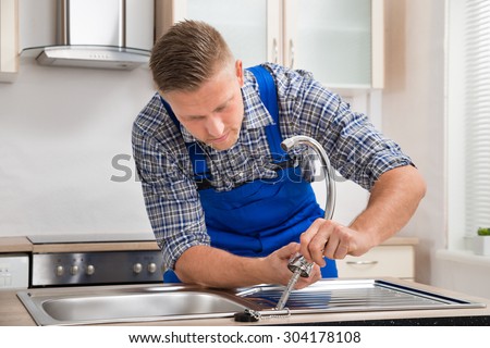 Young Repairman Installing Faucet Of Kitchen Sink In Kitchen Room