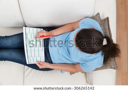 High Angle View Of Woman Sitting On Sofa With Calendar And Pen