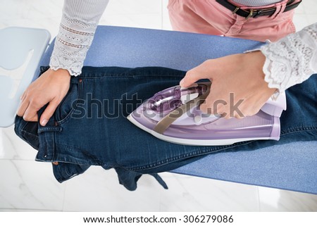 Close-up Of Woman Ironing Jeans On Ironing Board