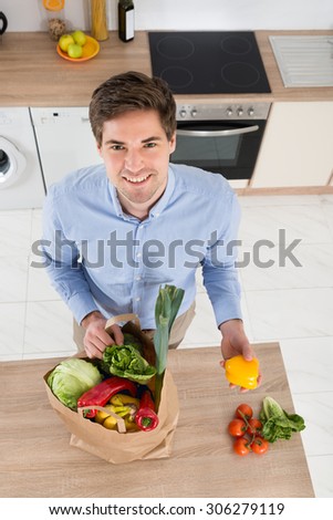 High Angle View Of Man Removing Vegetables From Grocery Bag In Kitchen