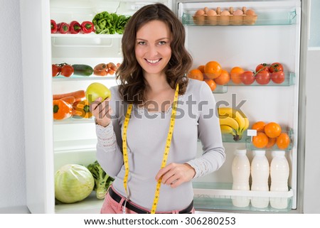Happy Woman With Measuring Tape And Green Apple Near The Open Refrigerator With Healthy Food