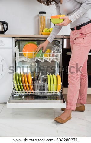 Woman Standing In Kitchen Removing Bowls From Dishwasher