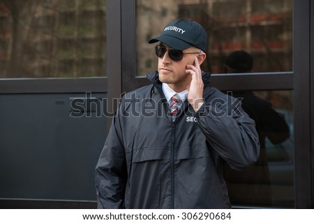 Young Security Guard Standing In Front Of The Glass Door Entrance