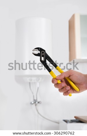 Close-up Person Hands Holding Wrench In Front Of Electric Boiler Attached On White Wall