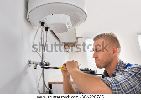 Male Repairman Repairing Electric Boiler With Wrench At Home