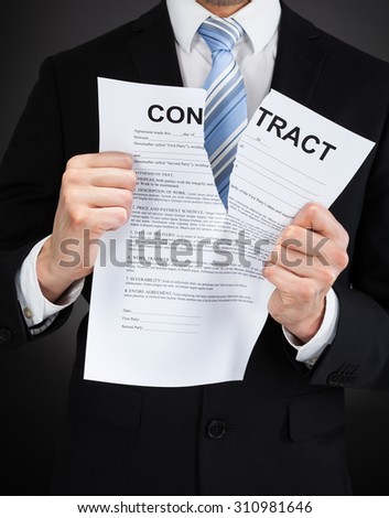 Midsection of businessman tearing contract paper against black background