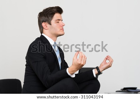 Young Businessman Doing Meditation At Desk In Office