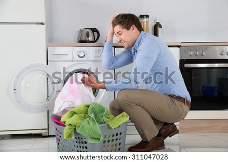 Man Near The Washing Machine With Laundry Basket Holding Stained Cloth In Kitchen