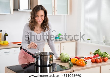 Young Woman Standing Near The Induction Cooker Cooking Meal In Kitchen