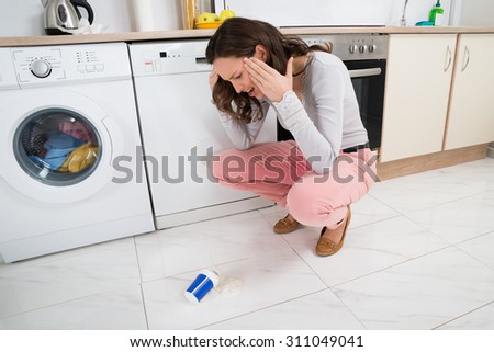 Frustrated Young Woman Looking At Yoghurt Fallen On The Floor In Kitchen Room