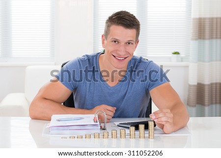 Happy Man Calculating Invoice With Coins At Desk In Living Room