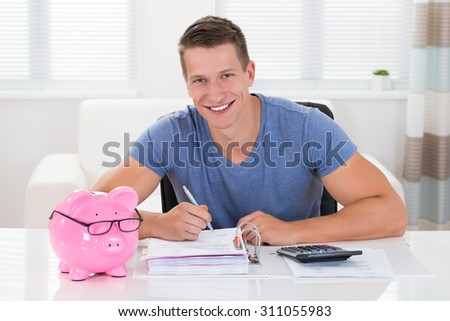 Happy Man With Piggybank Calculating Receipt At Desk