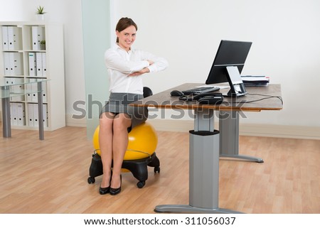 Young Happy Businesswoman Exercising On Pilates Ball In Office