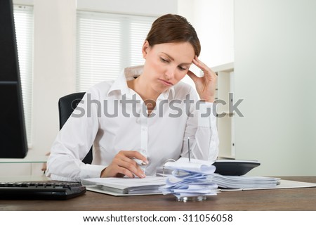Contemplated Young Businesswoman Calculating Receipts With Calculator In Office
