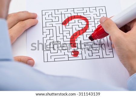 Close-up Of Person Hand With Question Mark On Labyrinth Maze Over Paper