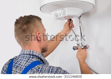 Young Male Worker Fixing Electric Boiler With Screwdriver