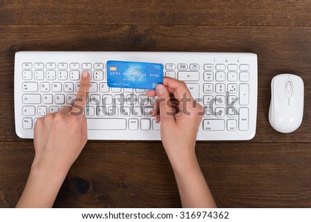 Close-up Of Person Hands With Credit Card And Computer Keyboard At Desk