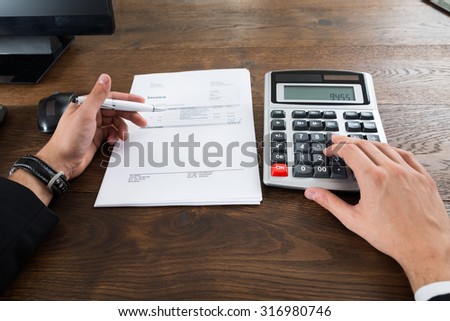 Close-up Of Businessperson Calculating Tax With Calculator In Office