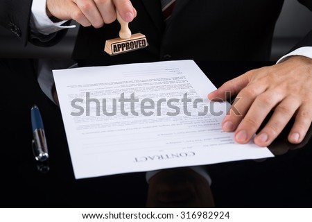 Close-up Of Businessperson Approving Contract Paper With Stamper