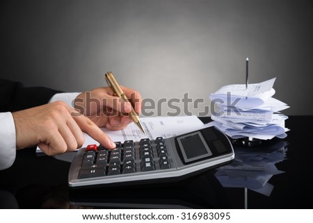 Close-up Of Businessperson Calculating Invoice With Calculator At Desk