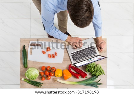 Young Man Chatting On Social Networking Site With Laptop On Countertop In Kitchen