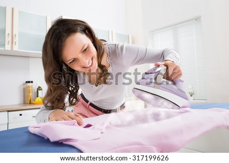 Happy Woman Ironing Cloth With Electric Iron In Kitchen
