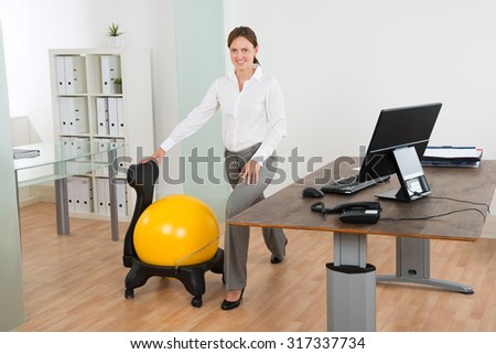 Young Happy Businesswoman Exercising With Pilates Ball On Chair In Office