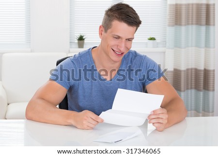 Happy Young Man Reading Letter At Desk