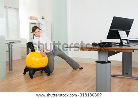 Young Happy Businesswoman Doing Fitness Exercise On Yellow Pilates Ball In Office