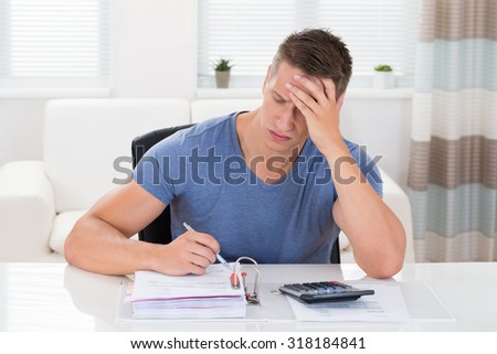 Young Stressed Man Calculating Finance At Desk