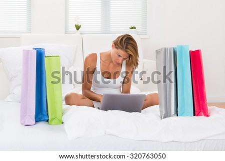 Young Woman Sitting On Bed Shopping Online On Laptop