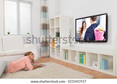 Young Woman Watching Movie While Lying On Carpet In Living Room