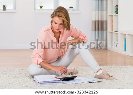 Young Woman Sitting On Carpet Calculating Invoices With Calculator