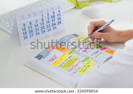 Close-up Of Businessman With Calendar Writing Schedule In Diary